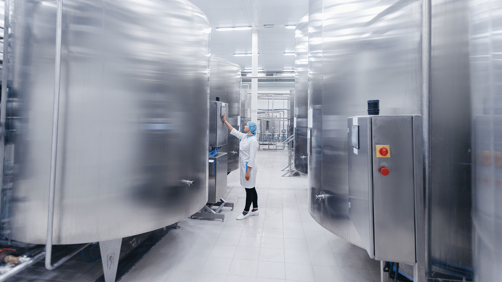 Worker operates a control panel next to machinery in a dairy processing plant.